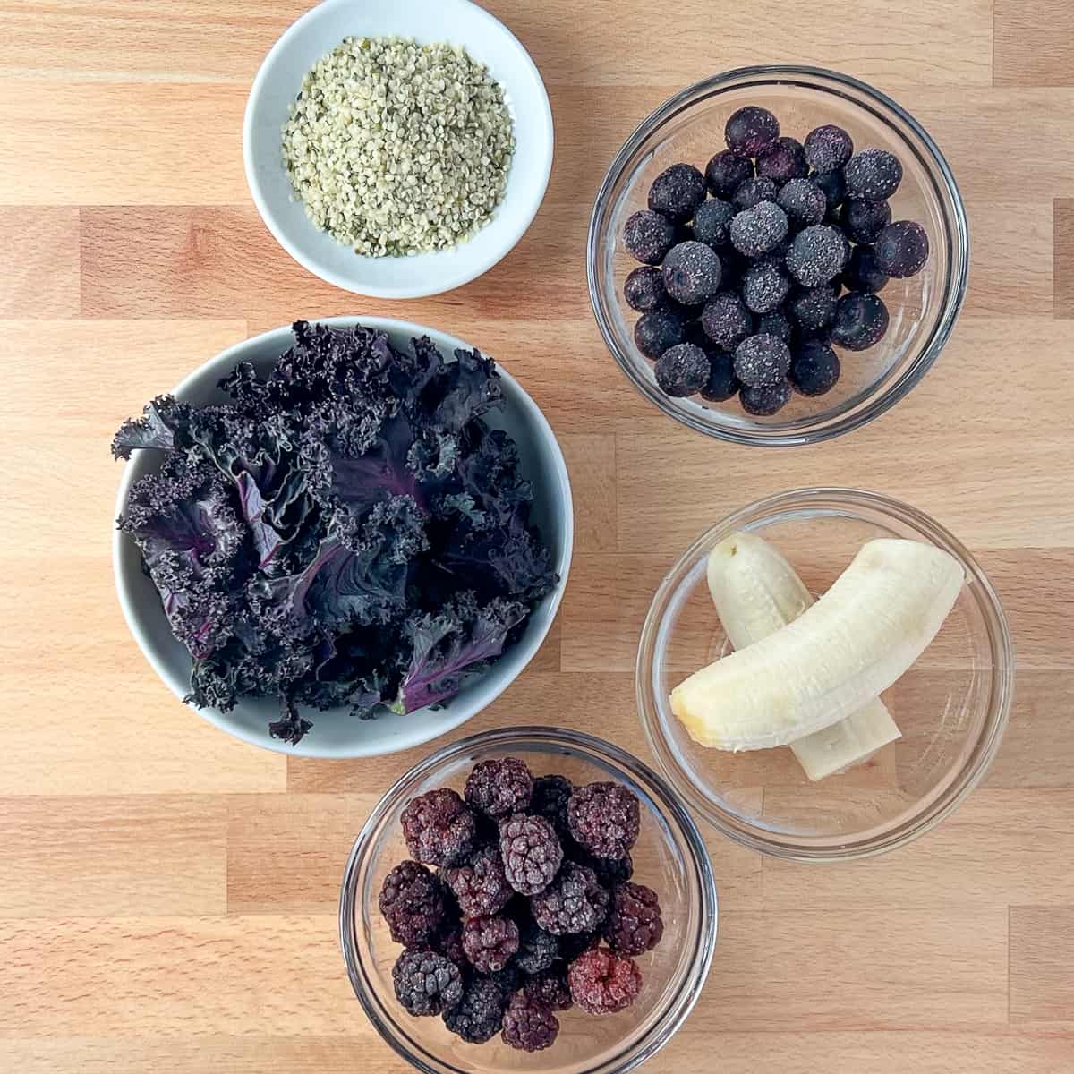 top view of the key ingredients in the superfood smoothie: hemp hearts, blueberries, kale, banana, blackberries.