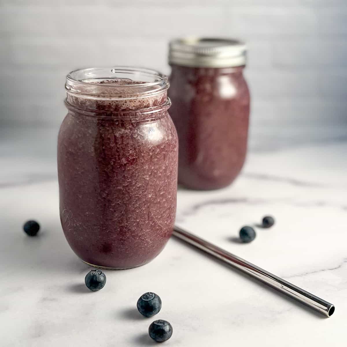 side view of superfood smoothie in two glass mason jars with a few loose blueberries scatter on the surface
