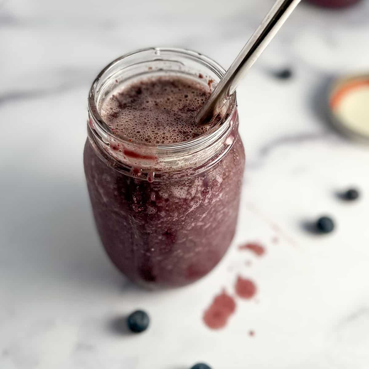 top side view of superfood smoothie in a glass mason jar with a metal straw sticking out of it.