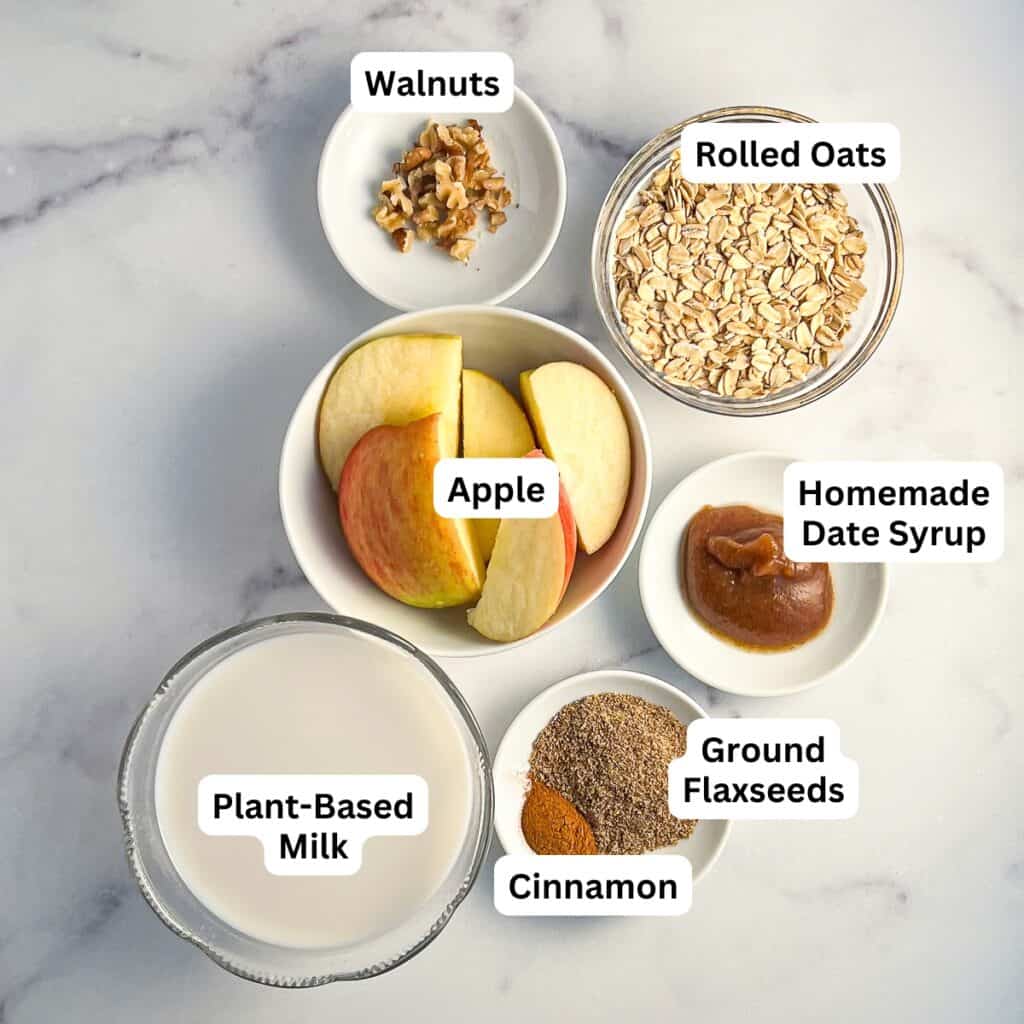 Ingredients for apple smoothie: rolled oats, cored apple, date syrup, ground flaxseed, cinnamon, unsweetened plant based milk, chopped walnuts.
