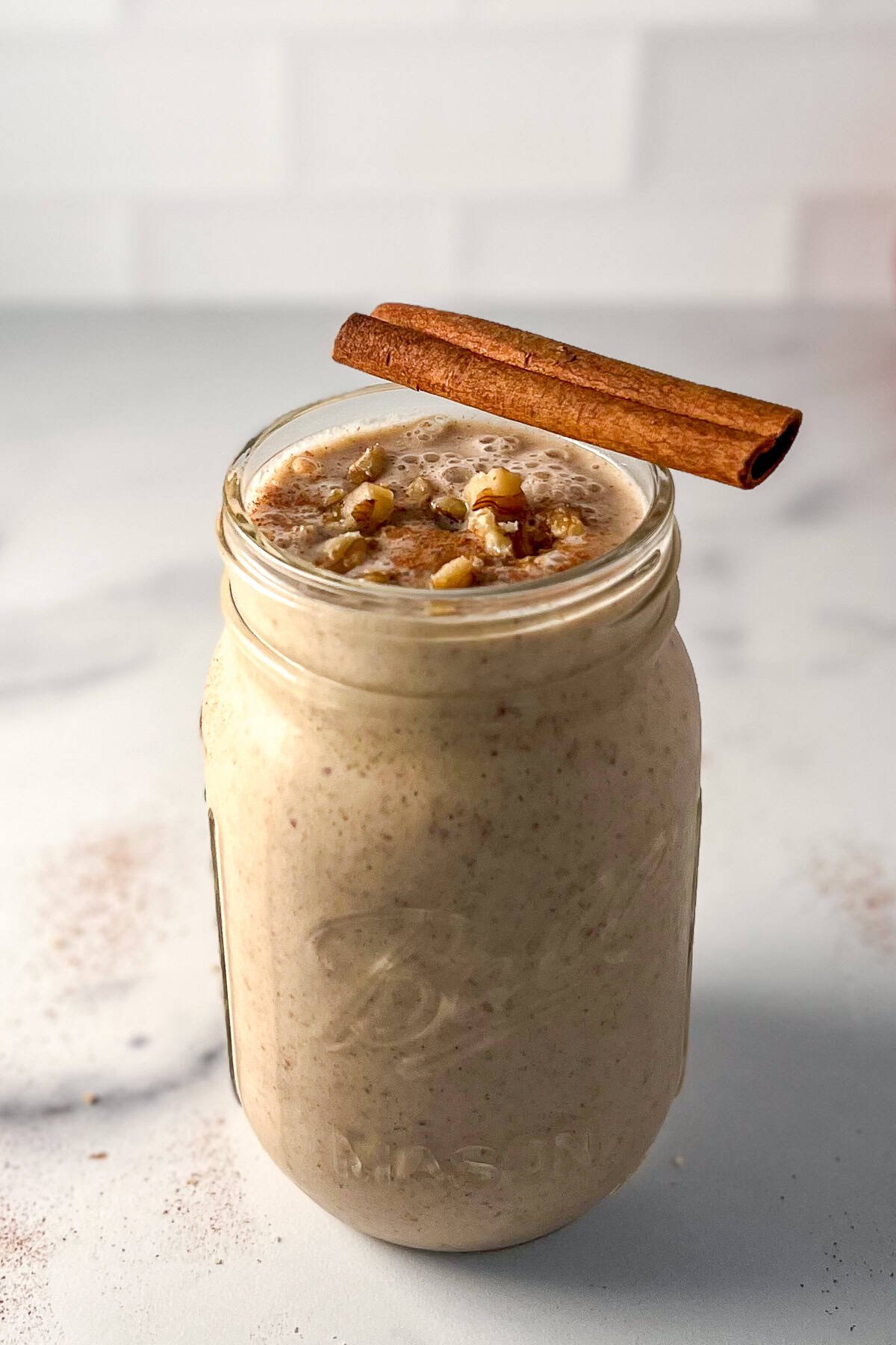 Apple smoothie in a mason jar with a cinnamon stick balanced on the rim.