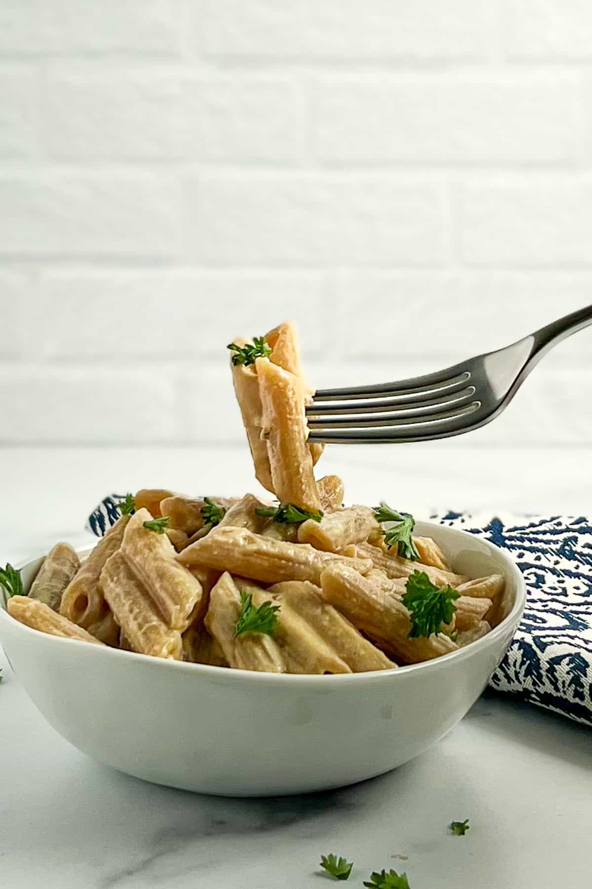 side view close up of tahini penne pasta with fresh parsley and a fork