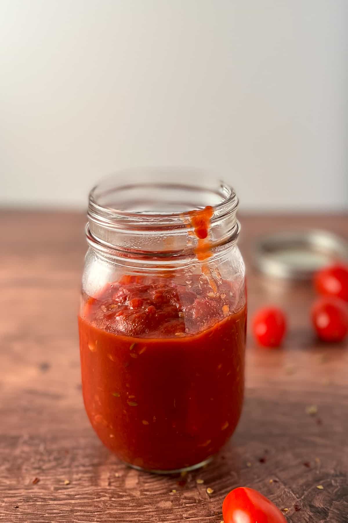 side view of easy homemade pizza sauce in a glass mason jar with loose grape tomatoes blurred in the background