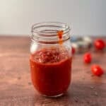 Homemade pizza sauce in a glass mason jar with loose grape tomatoes blurred in the background.