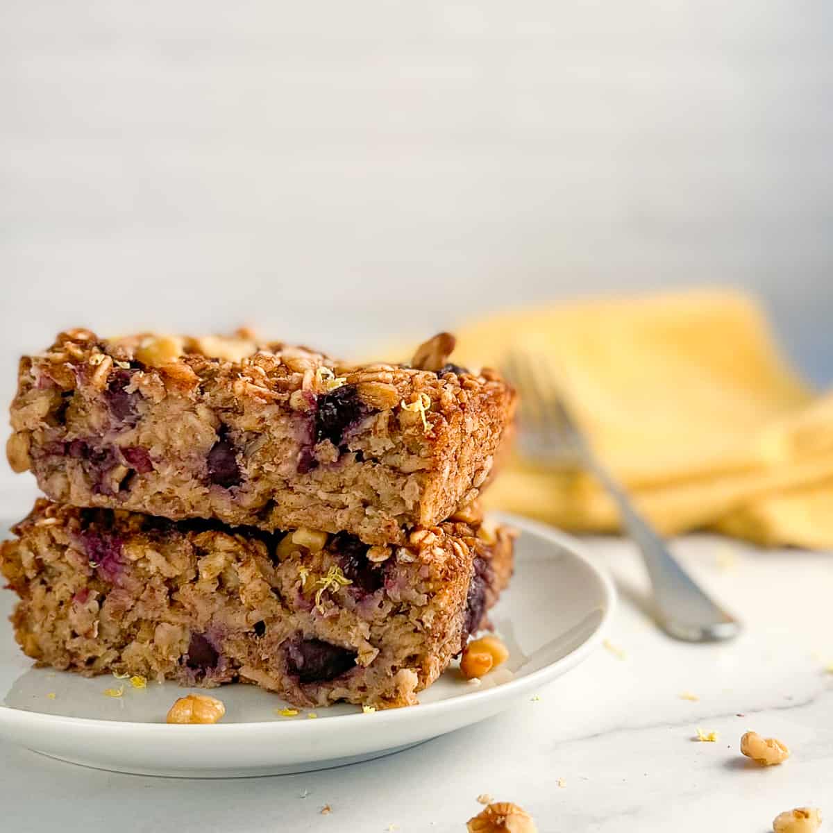 side view close up of lemon blueberry baked oatmeal for one on a white plate with fork and yellow napkin blurred in the background