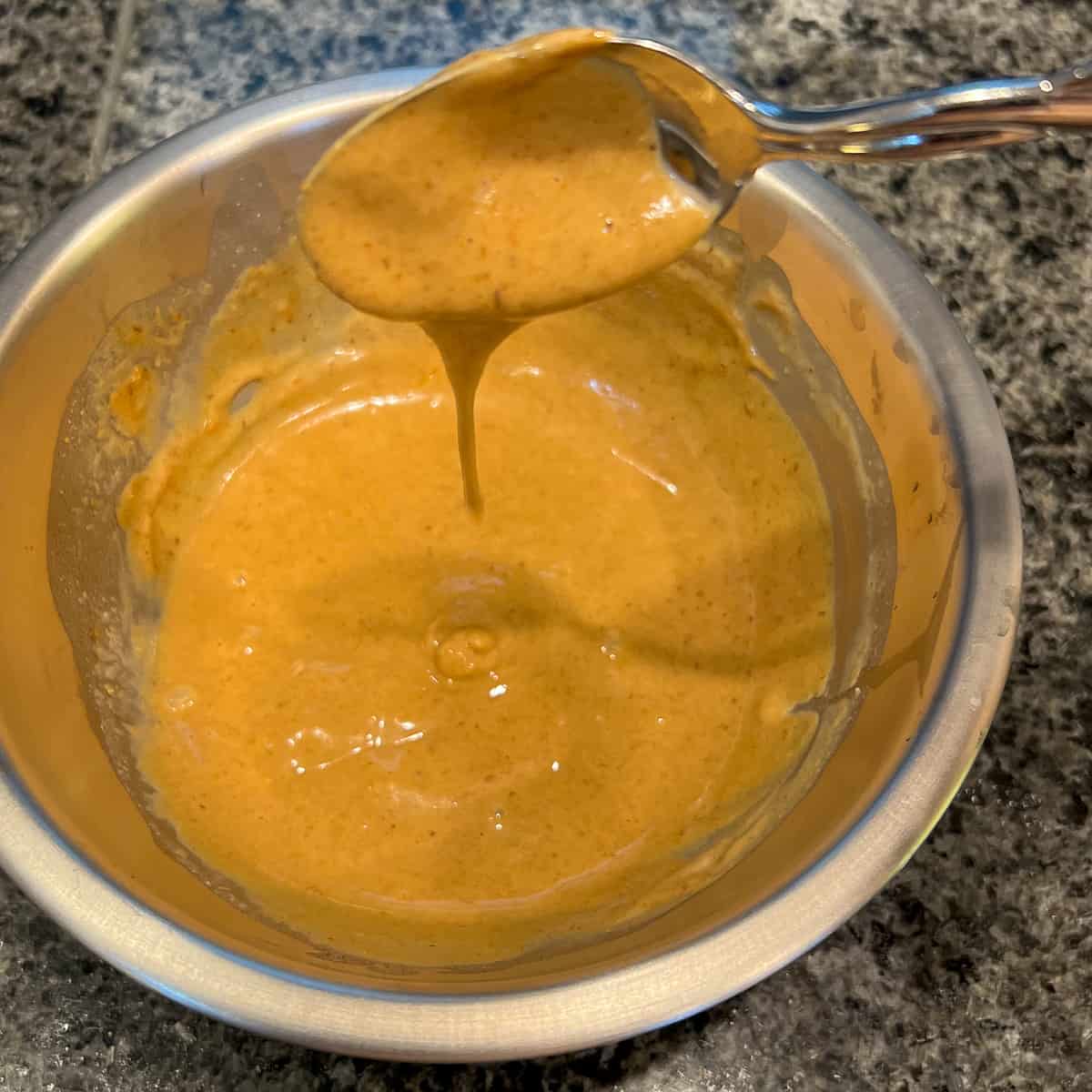 Creamy peanut sauce in a small mixing bowl with a spoon coming out.