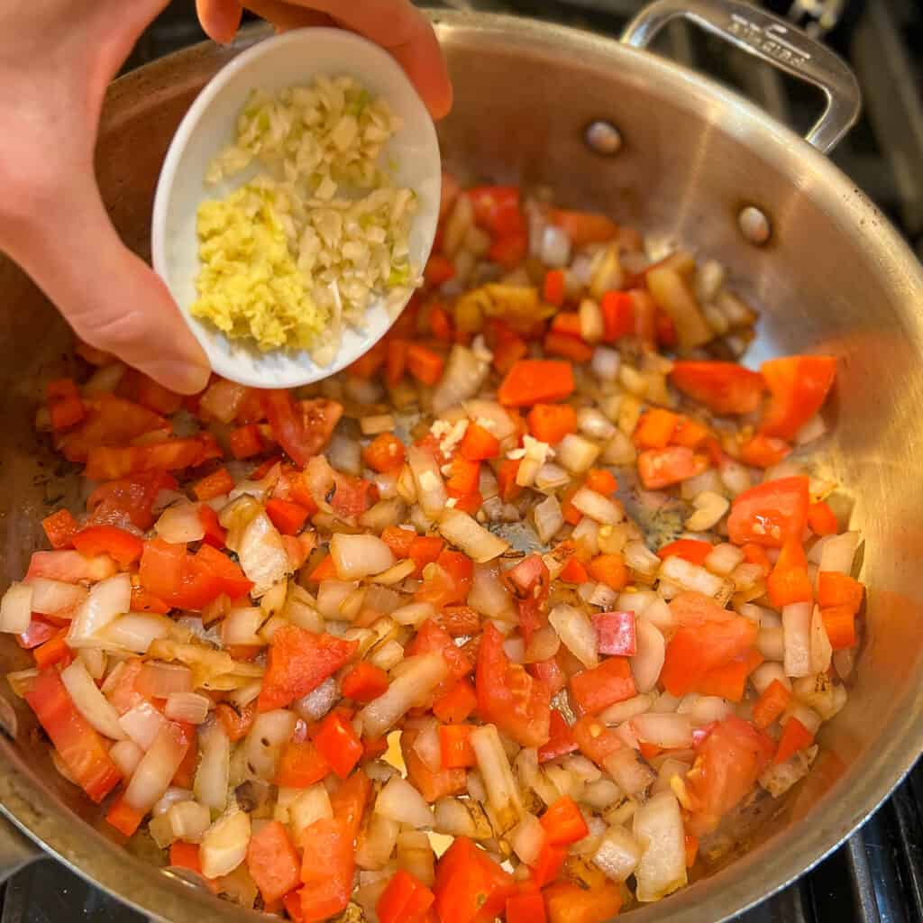 Chopped garlic being added to a skillet with onions, red pepper and tomato.