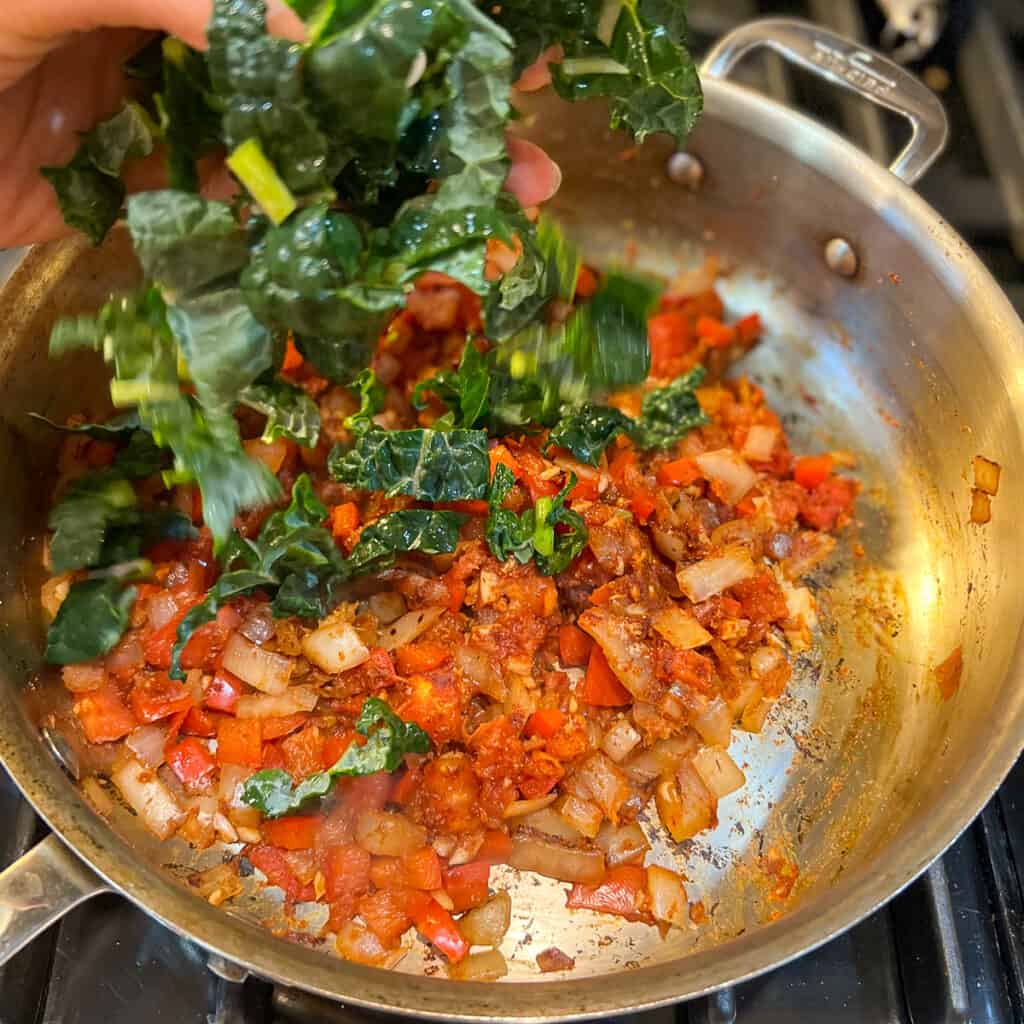 Chopped kale being added to a skillet with sautéed vegetables. 