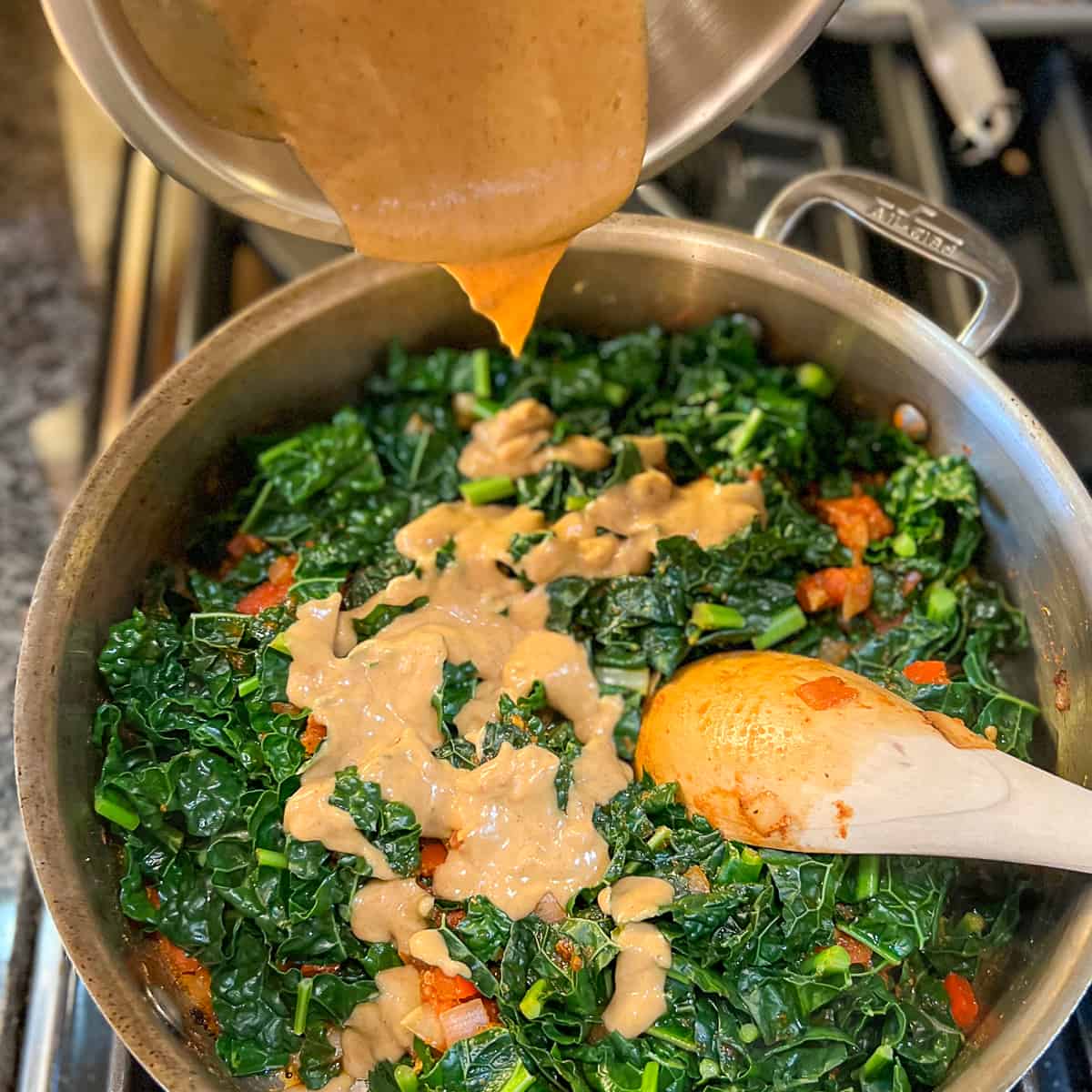 Peanut butter sauce being added to the skillet with cooked greens.