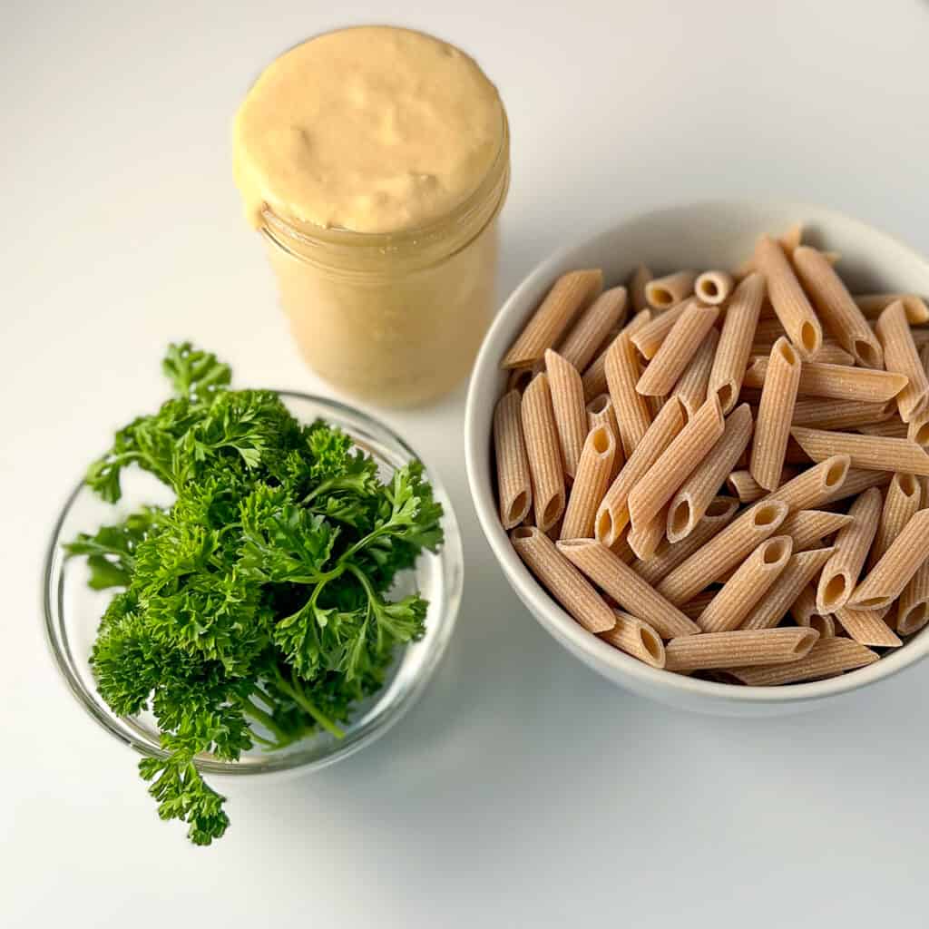 top view of the ingredients for tahini pasta: tahini pasta sauce, dried pasta and fresh herbs (parsley).