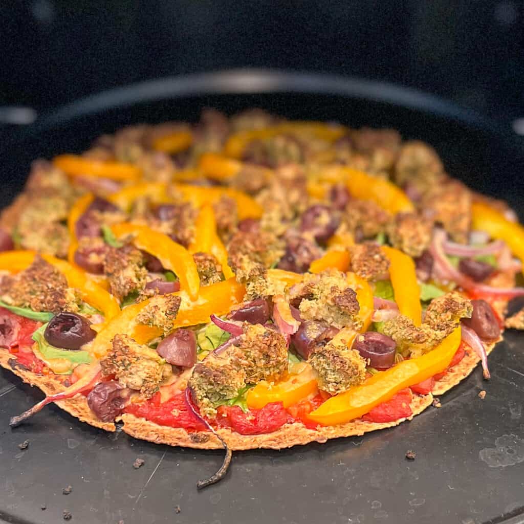 side view of a baked vegan mediterranean pizza coming out of the oven
