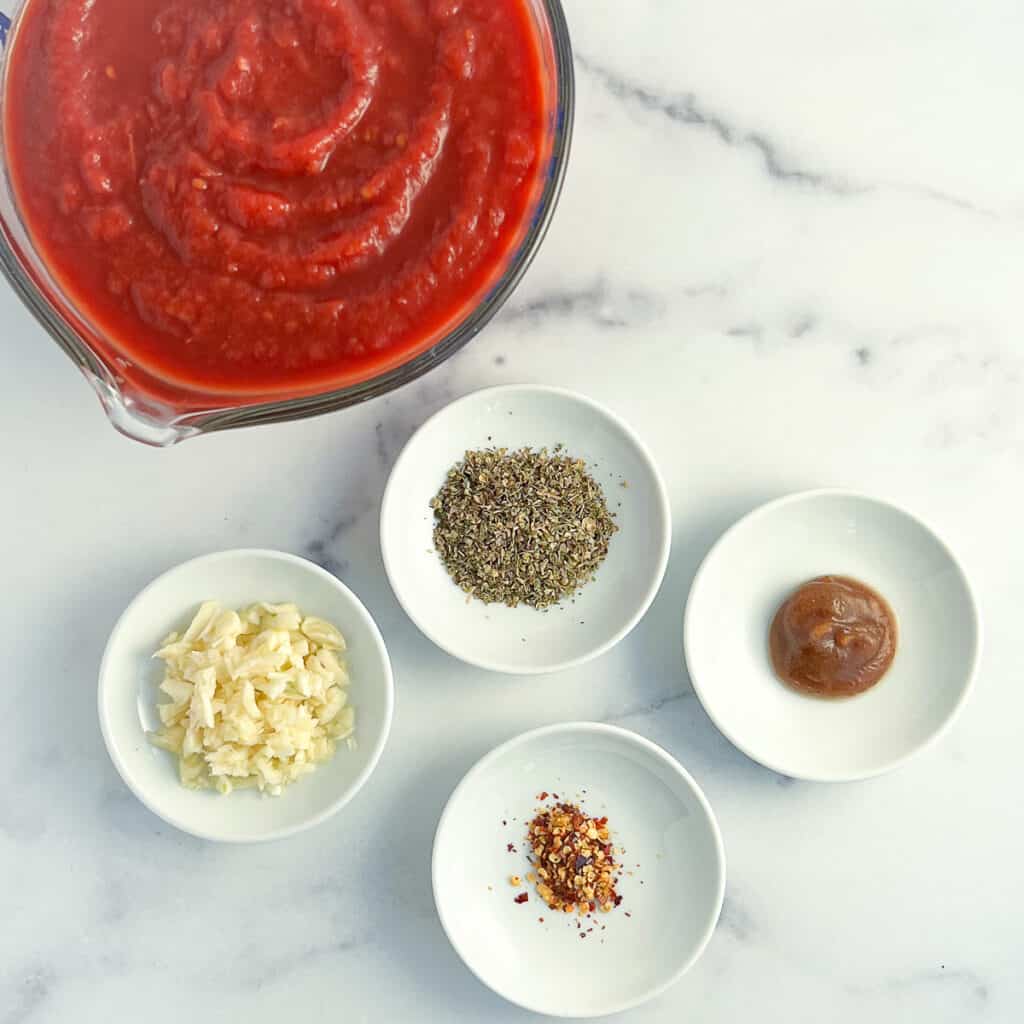 top view of key ingredients for spaghetti sauce: crushed tomatoes, italian seasoning blend, garlic, date syrup and crushed red peppers
