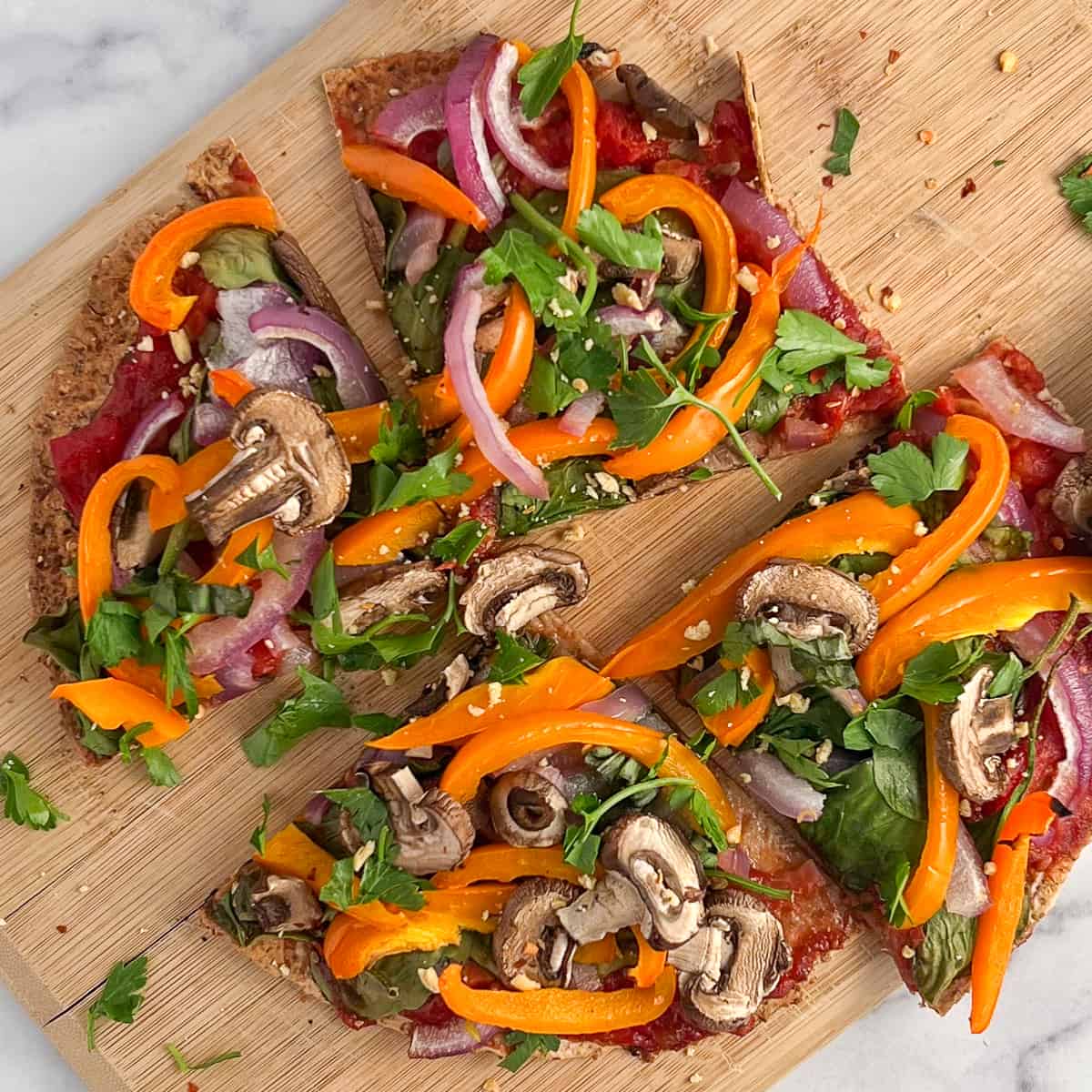 top view close up of veggie pizza cut into 4 slices on a wooden cutting board