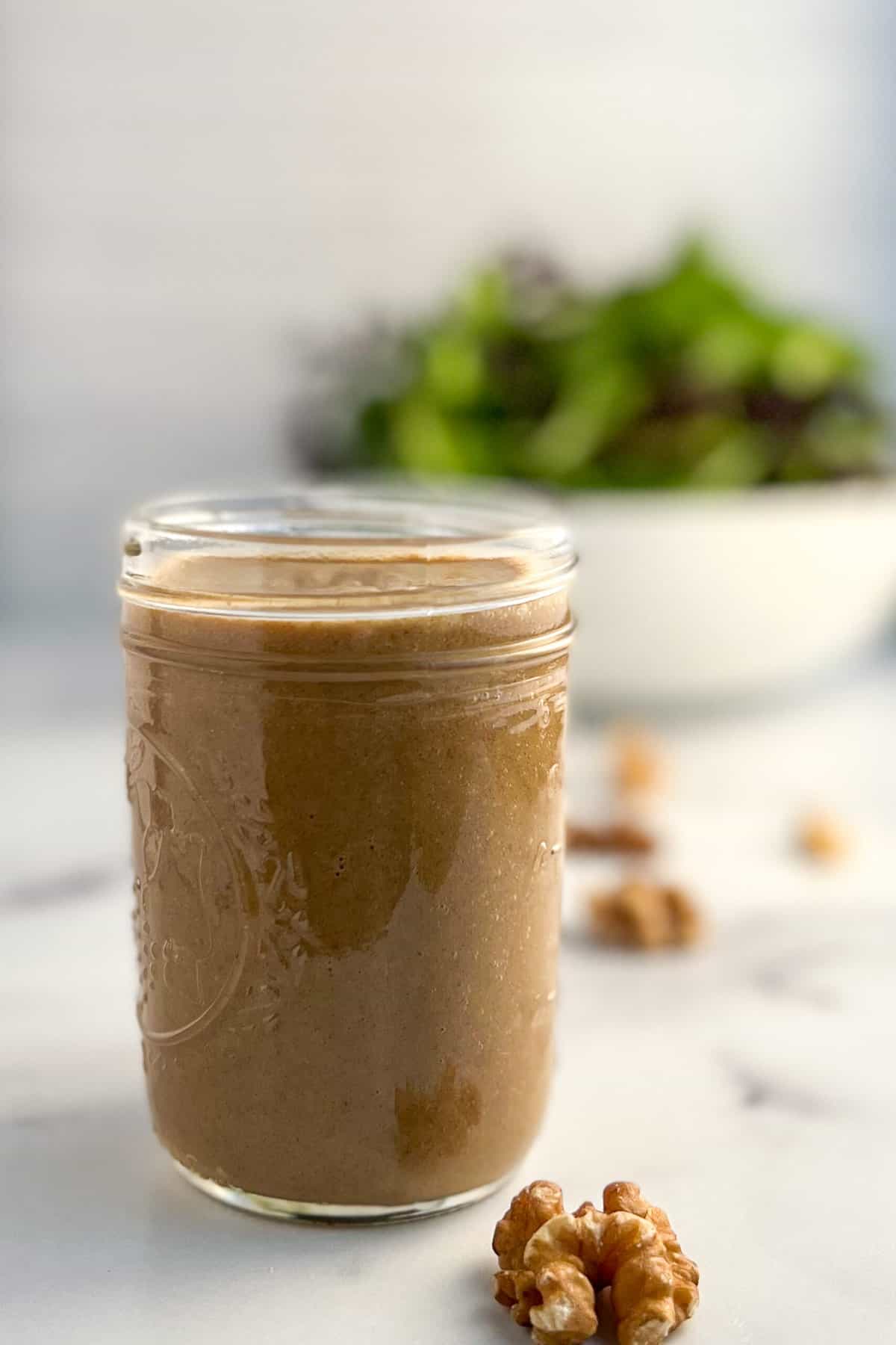 side view close up of walnuts salad dressing in a glass mason jar with loose walnuts and salad greens blurred in the background