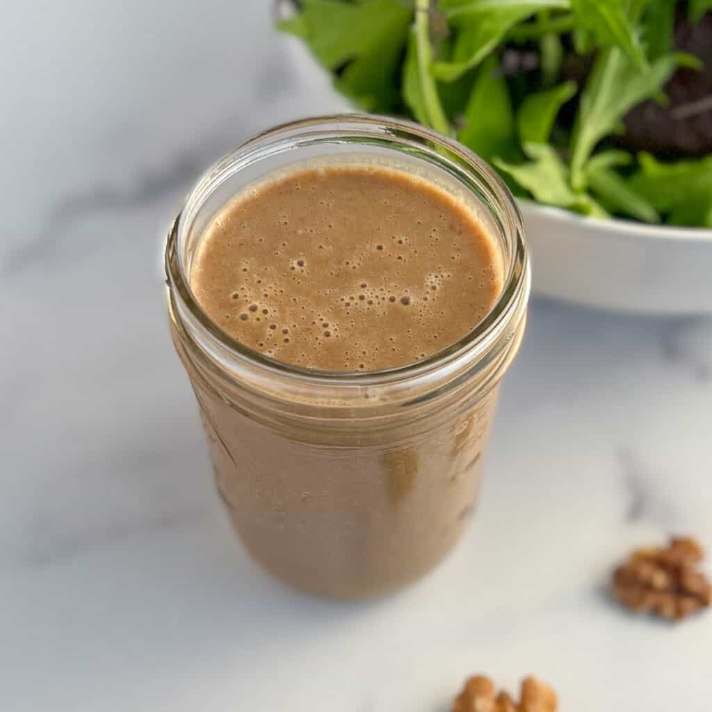 side top view of the walnut salad dressing in a glass mason jar with loose walnuts and salad greens blurred in the background