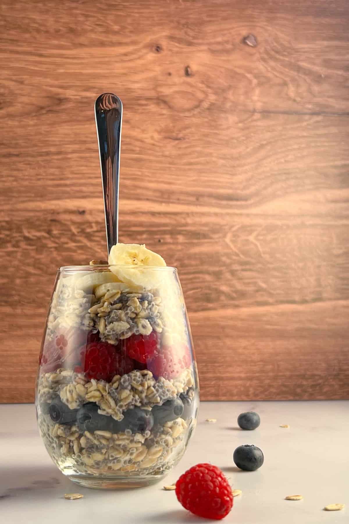 side view of overnight oats layered in a glass with blueberries, raspberries, banana