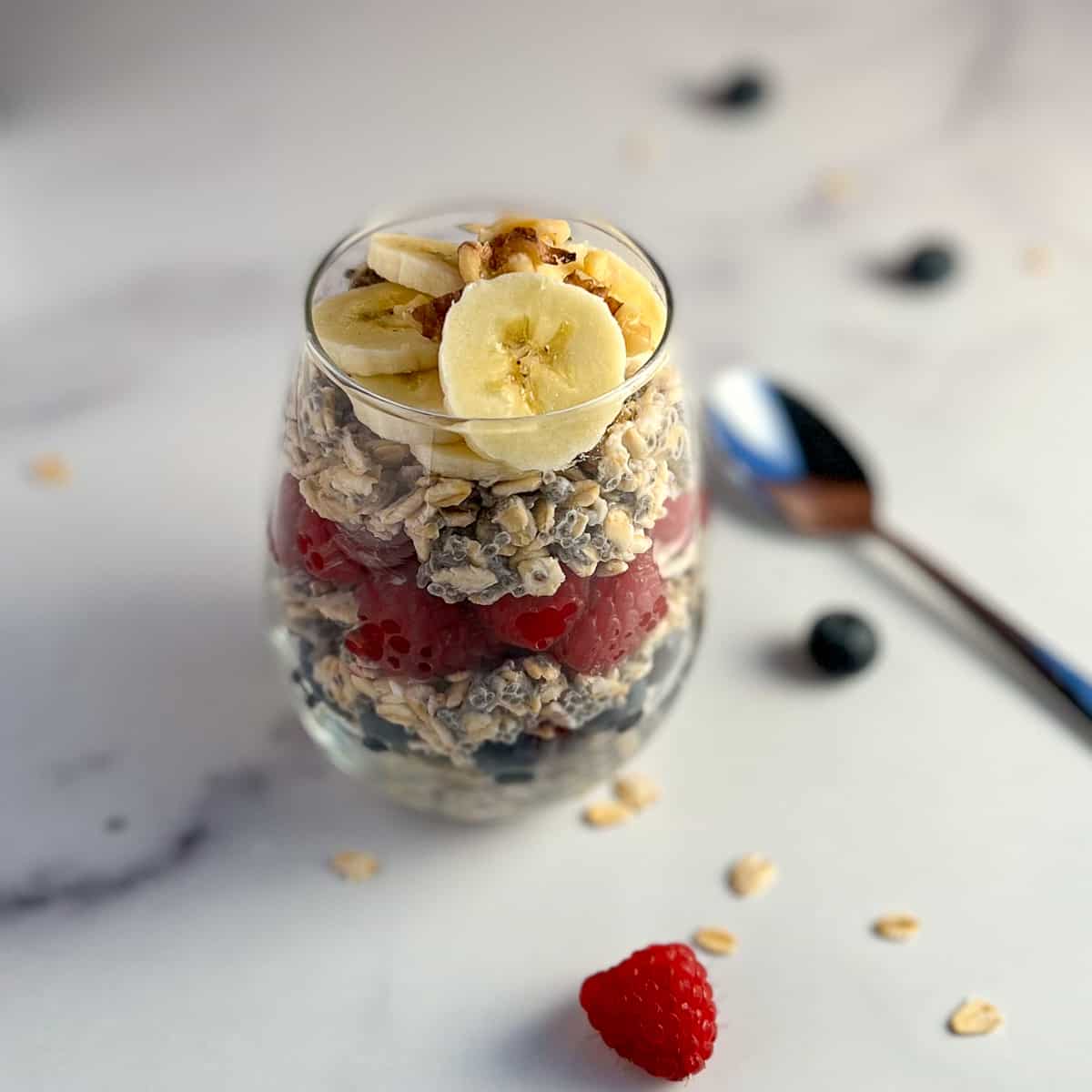 side top view of overnight oats with bananas, raspberries, blueberries and chia seeds with a spoon blurred in the background