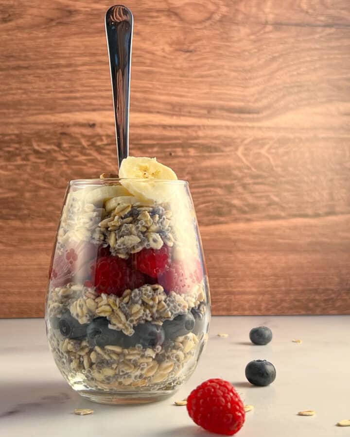 side view of overnight oats layered with berries and banana in a glass with spoon sticking out