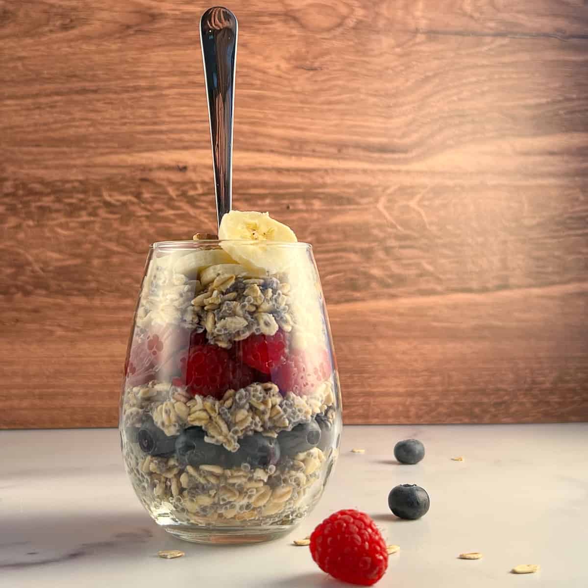 side view of overnight oats layered with berries and banana in a glass with spoon sticking out