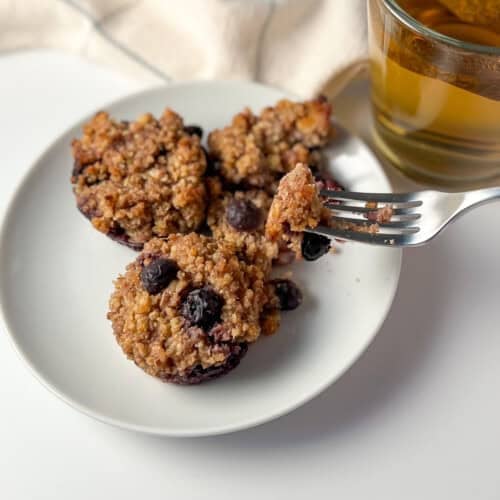 top side view of flourless blueberry millet muffins on a white plate with a fork with a cup of tea on the side