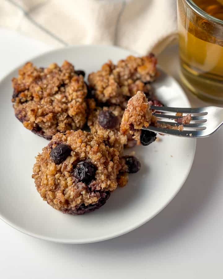 top side view of flourless blueberry millet muffins on a white plate with a fork with a cup of tea on the side