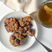 top view of 3 blueberry millet muffins on a white plate with a fork and cup of tea on the side
