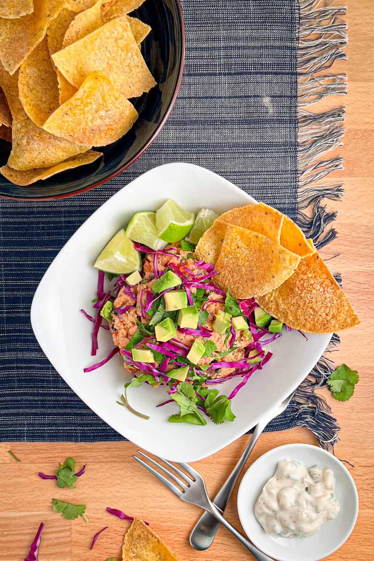 top view close of a bowl of deconstructed vegan fish tacos with vegan tuna salad topped with cabbage, avocado and cilantro. fresh lime, corn tortillas and vegan fish taco sauce on the side.