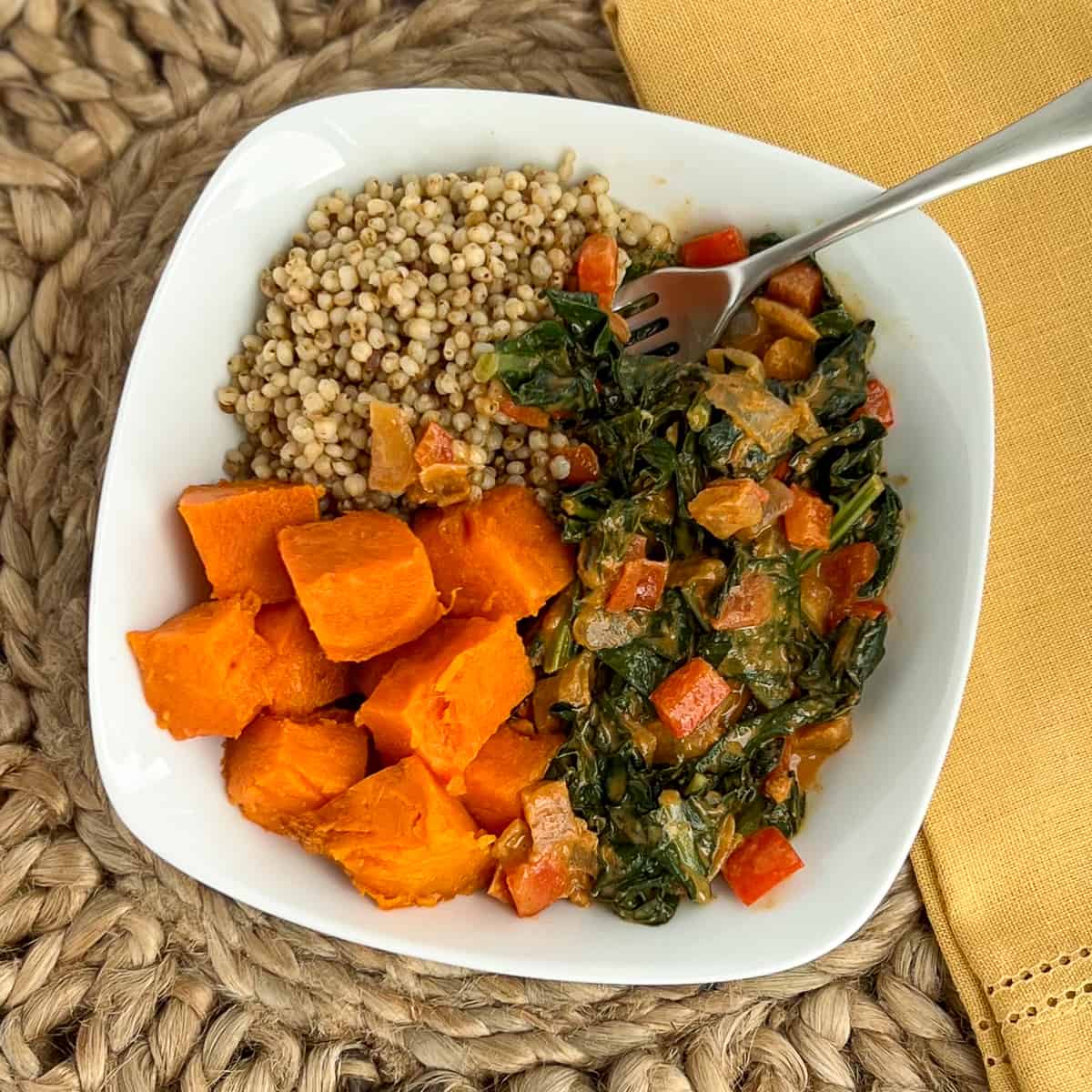 top view close up of peanut butter greens, sorghum and sweet potato in a white bowl with fork
