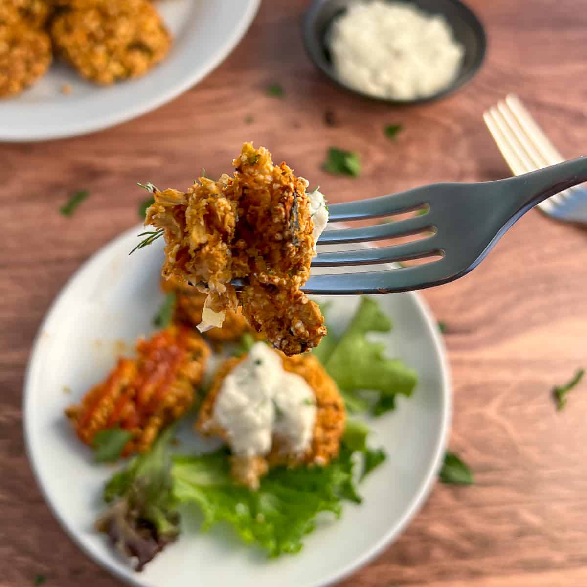 a bite of vegan crab cake on a fork with the plate of crab cakes blurred in the background
