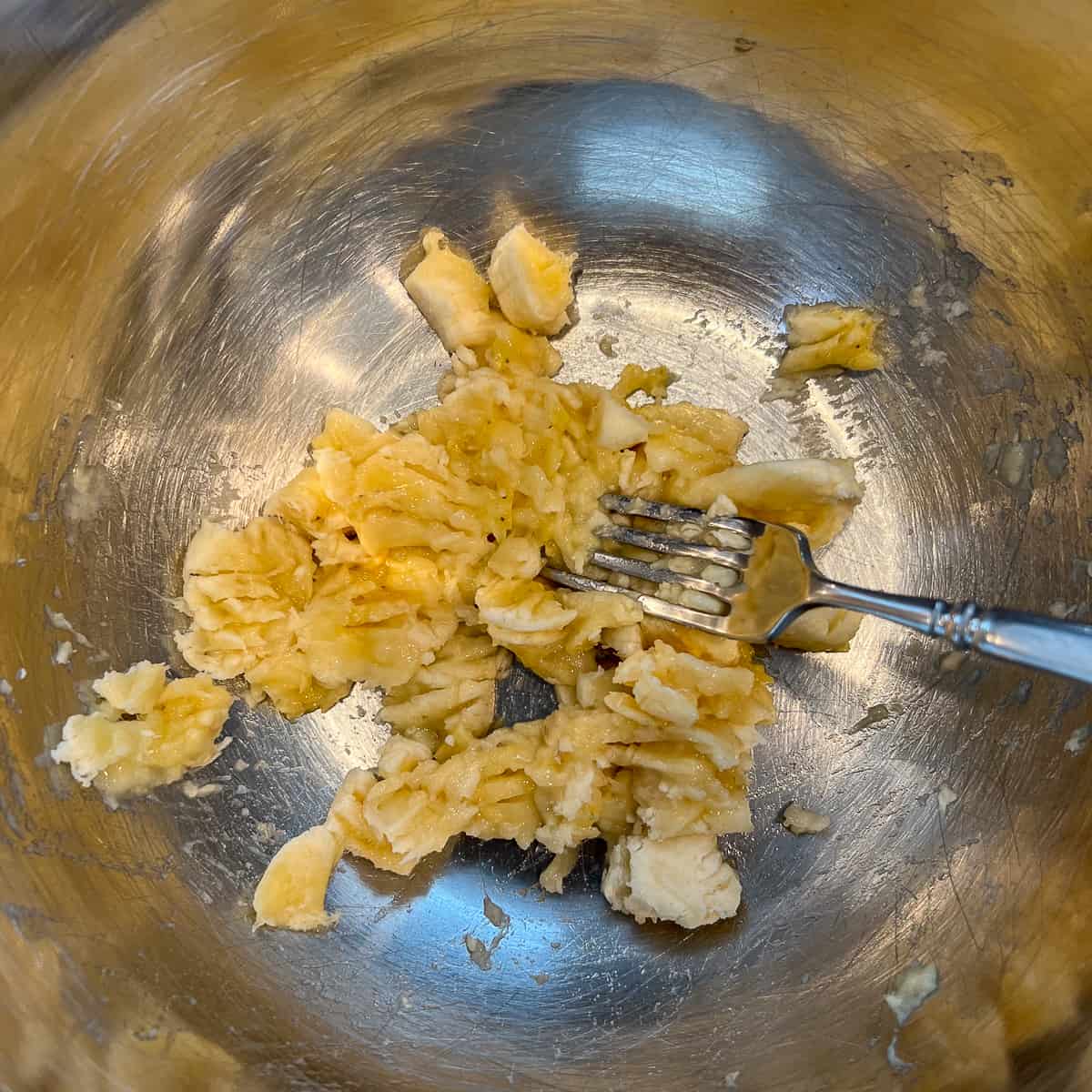 top view of a fork smashing a banana in a stainless mixing bowl