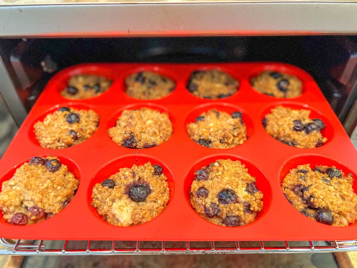 top side view of 12 blueberry millet muffins in a red silicone baking muffin tin baked and coming out of the oven