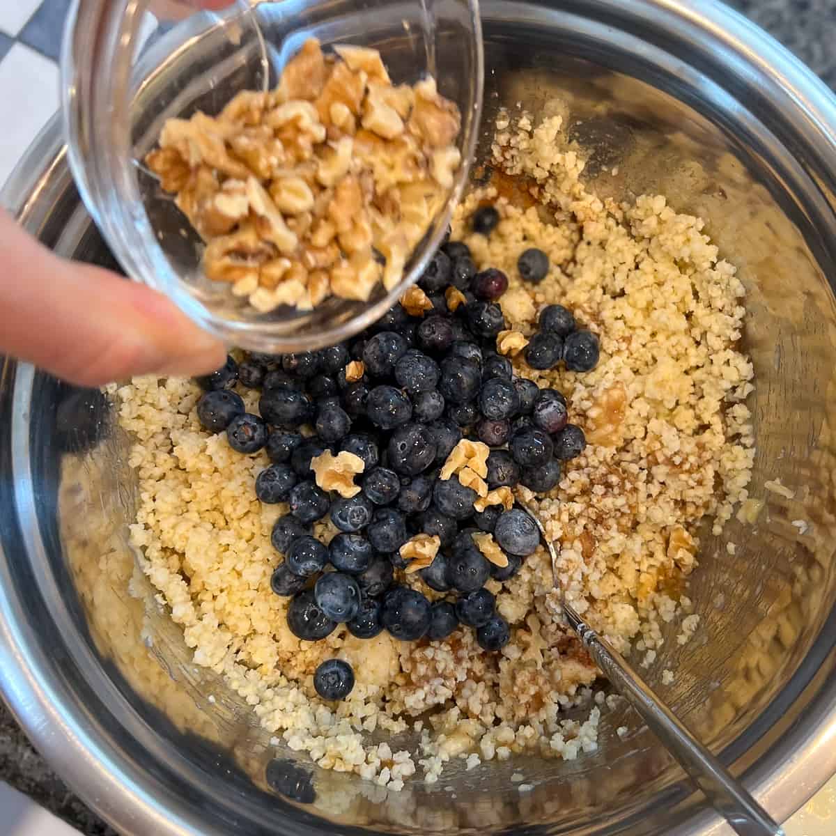 top view of mixing bowl with millet muffin batter, blueberries and walnuts being added