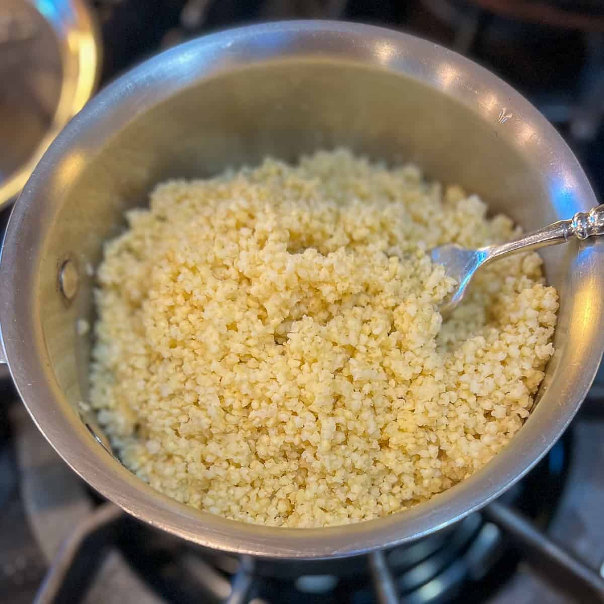 top side view close up of perfectly cooked millet in a medium pot being fluffed with a fork 