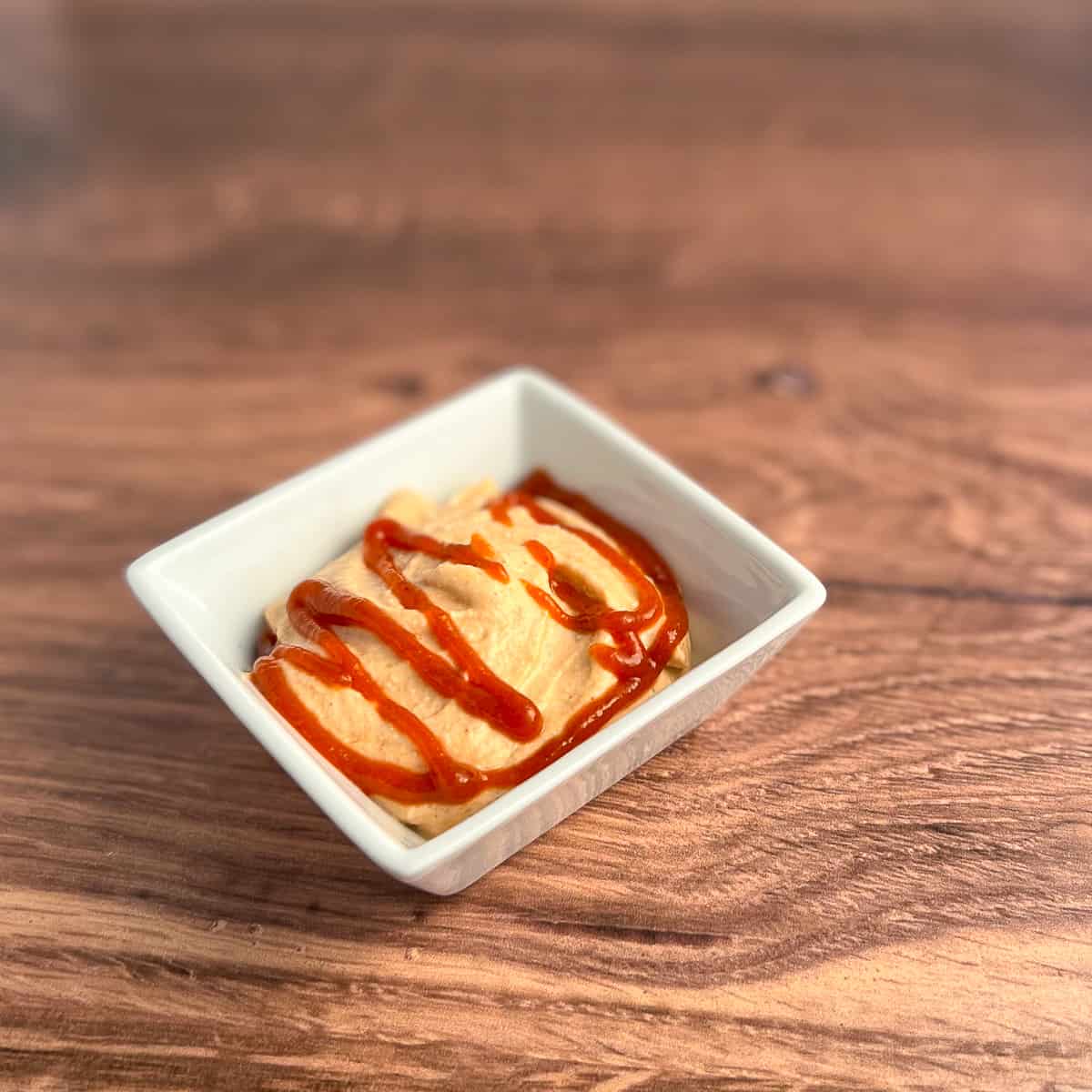 top view close up of sriracha vegan mayo in a square white bowl against a wooden surface