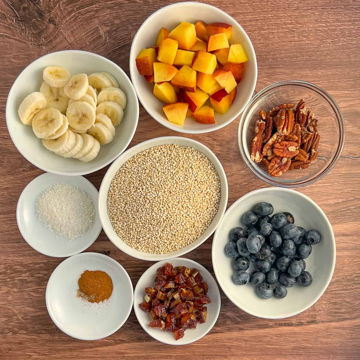 top view of ingredients for the vegan quinoa breakfast bowl: peaches, banana, pecans, quinoa, shredded coconut, blueberries, dates, cinnamon, cardamom