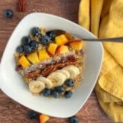 top view of vegan quinoa breakfast bowl in a square white bowl with a spoon and yellow napkin on the side
