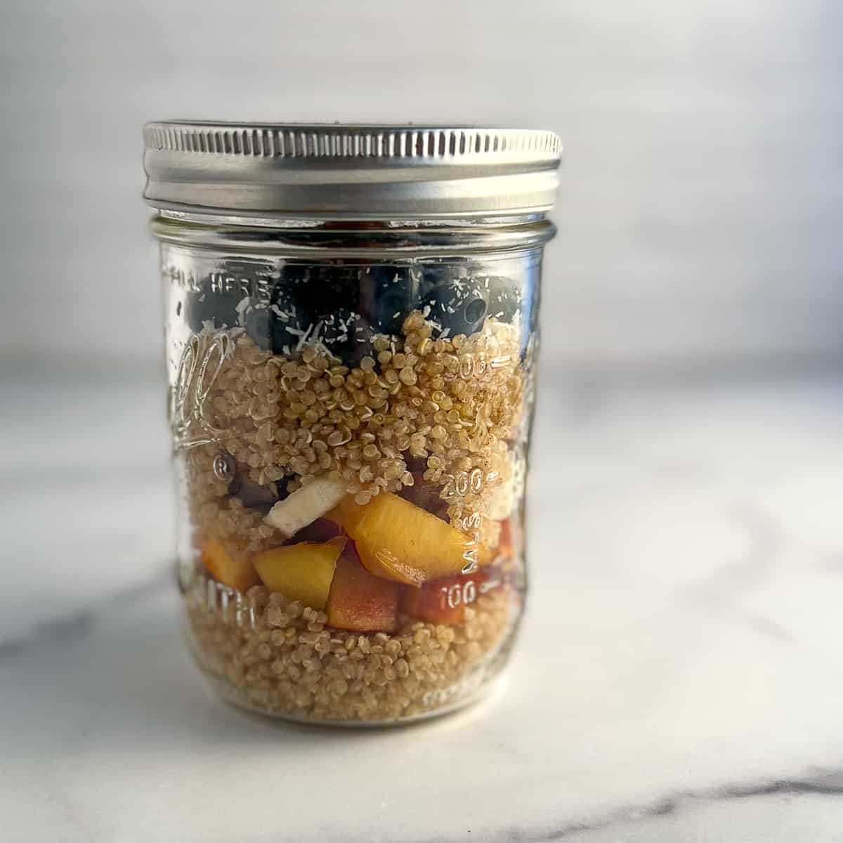 side view of the quinoa breakfast bowl ingredients layered in a glass mason jar with lid to show it can be meal prepped in advance