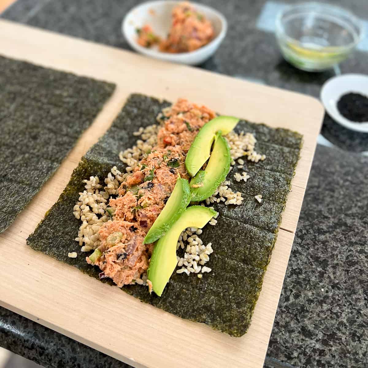 nori sheet with brown rice, vegan tuna salad, sliced avocado open on a wooden cutting board