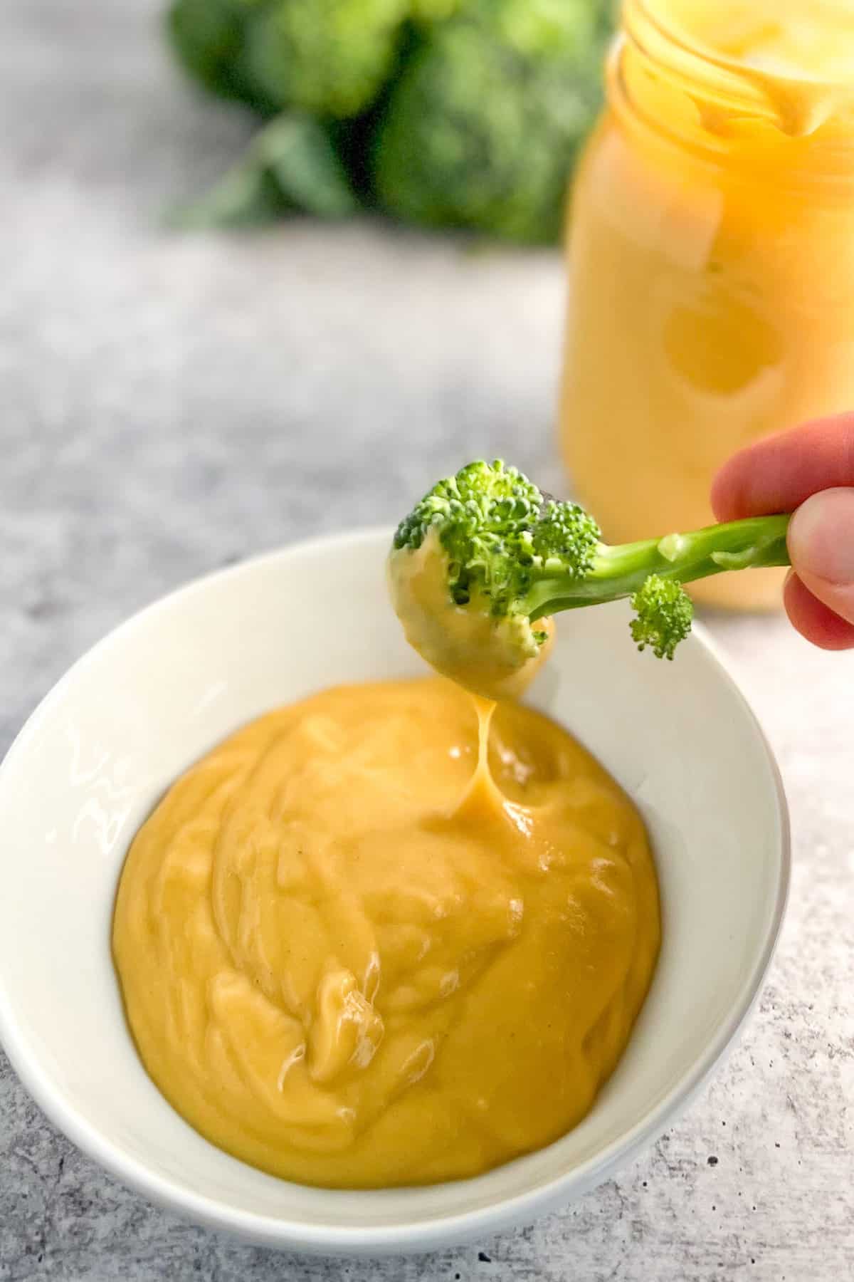 side view of broccoli floret being dipped in a small bowl of vegan cheese sauce.