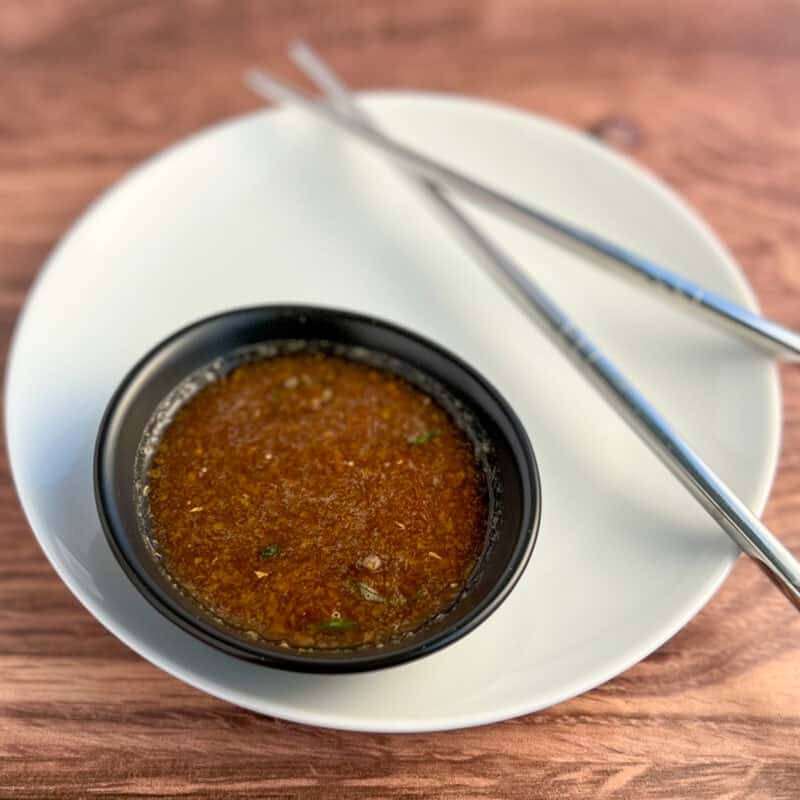 top side view of wasabi and ginger sauce in a small black bowl sitting on a round white plate with stainless steel chopsticks on the side