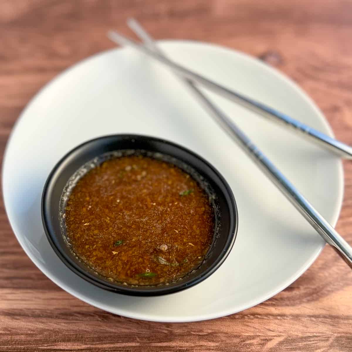 top side close up of wasabi and ginger dipping and stir fry sauce in a small black bowl sitting on a round white plate and stainless steel chopsticks on the side