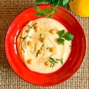 top view close up garlic hummus in a red bowl with fresh parsley on top.