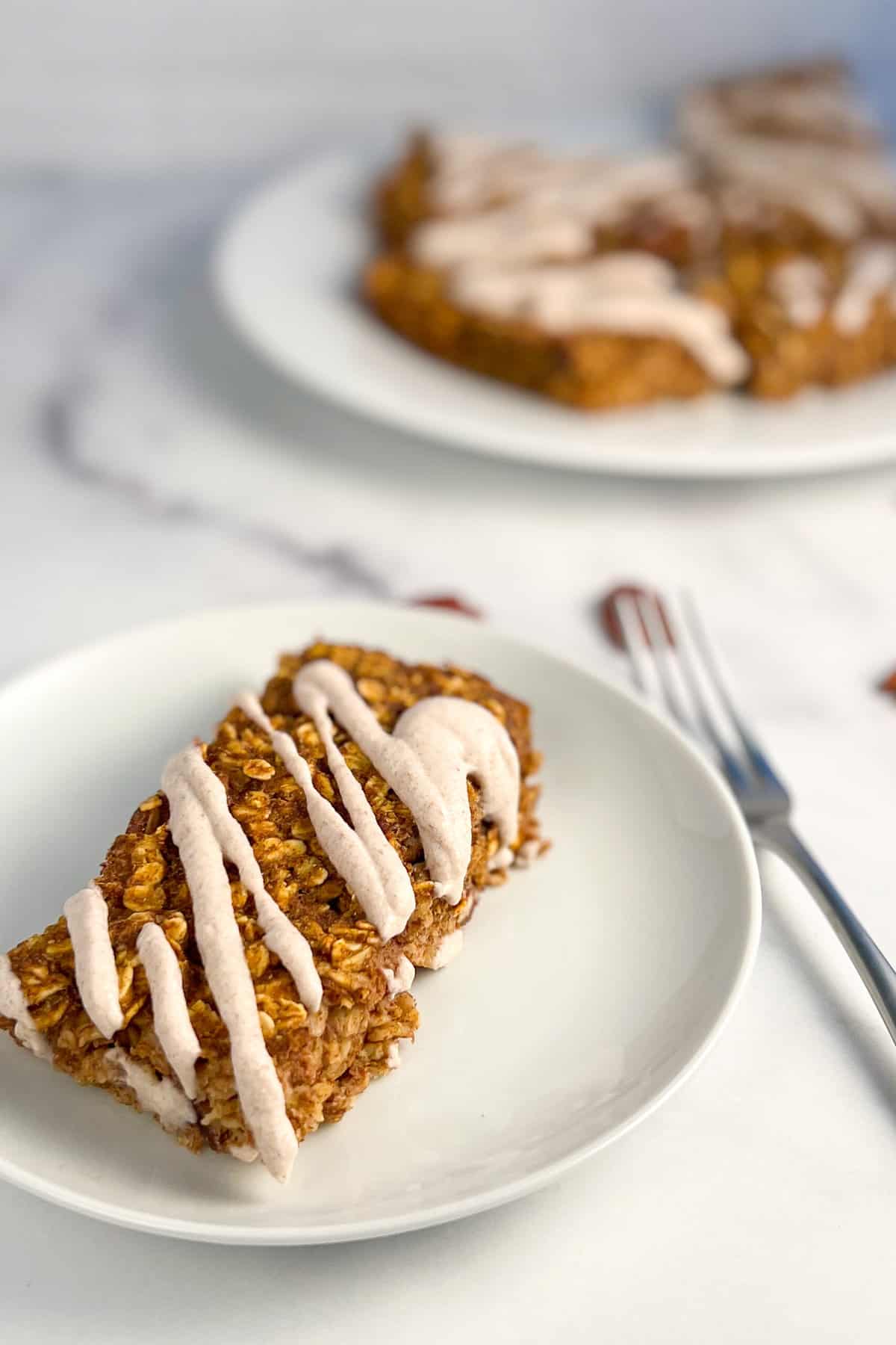top side view of a pumpkin oatmeal bar on a round white plate with for and plate of several bars blurred in the background
