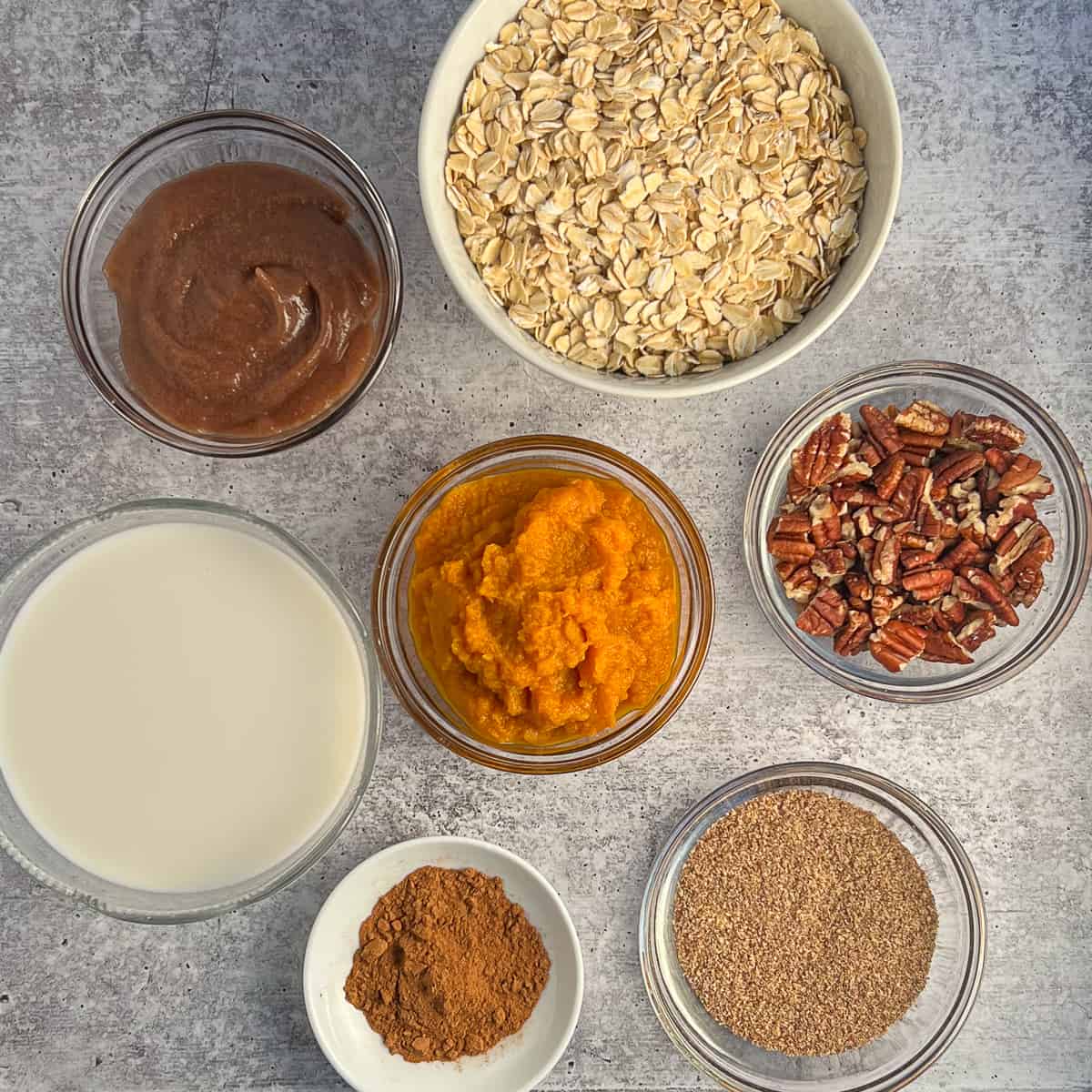 top view of the key ingredients for pumpkin oatmeal bars: rolled oats, pumpkin puree, pumpkin pie spice, ground flaxseed, pecans, unsweetened almond milk.