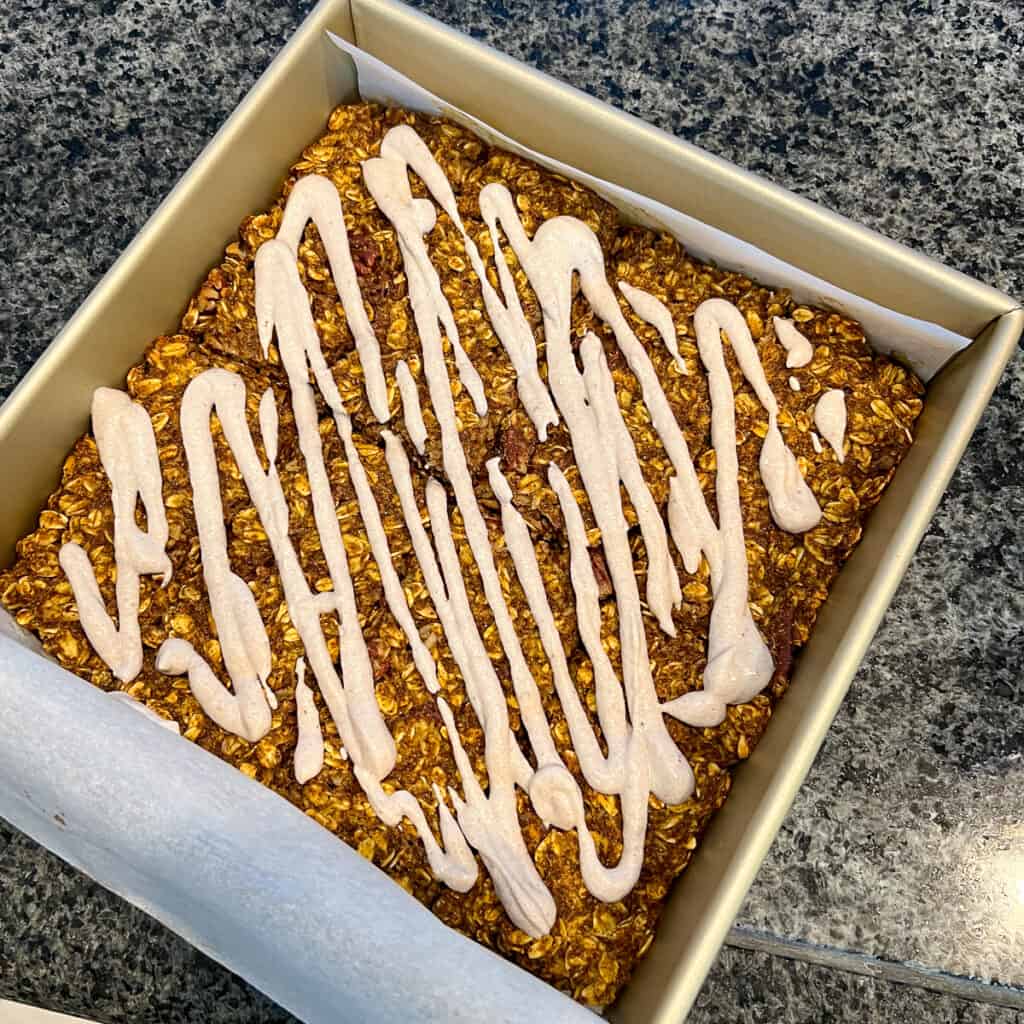 Pumpkin oatmeal bars in the pan after baking with sweet cashew cream drizzled on top.
