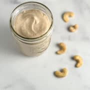 top side view of sweet cashew cream in a glass mason jar with loose cashews blurred in the background