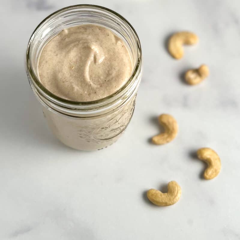 top side view of sweet cashew cream in a glass mason jar with loose cashews blurred in the background