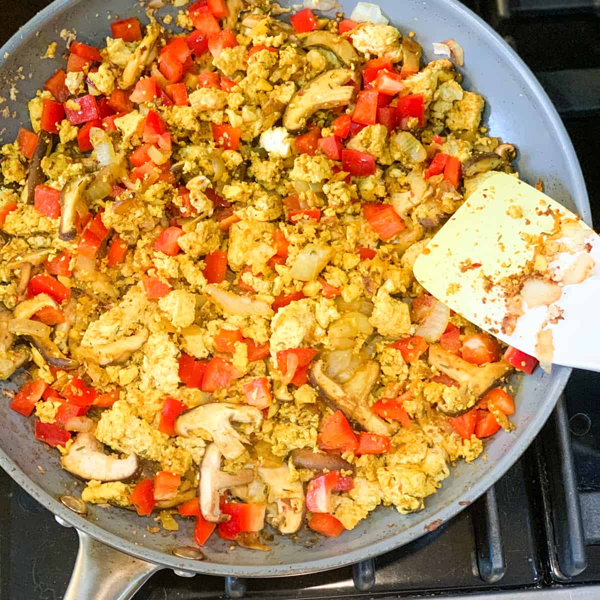 Top view and close up of a skillet with with tofu, mushrooms, red bell pepper, onion and garlic 