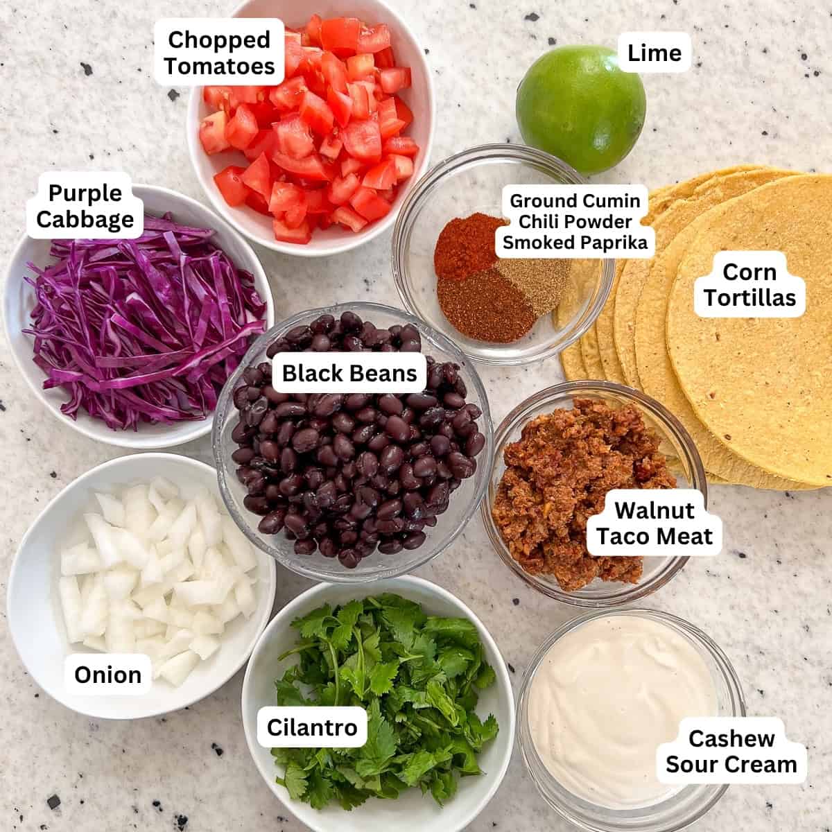 Black Bean Taco Ingredients: chopped tomato, lime, corn tortillas, walnut taco meat, cashew sour cream, black beans, cilantro, onions, purple cabbage, and spices.
