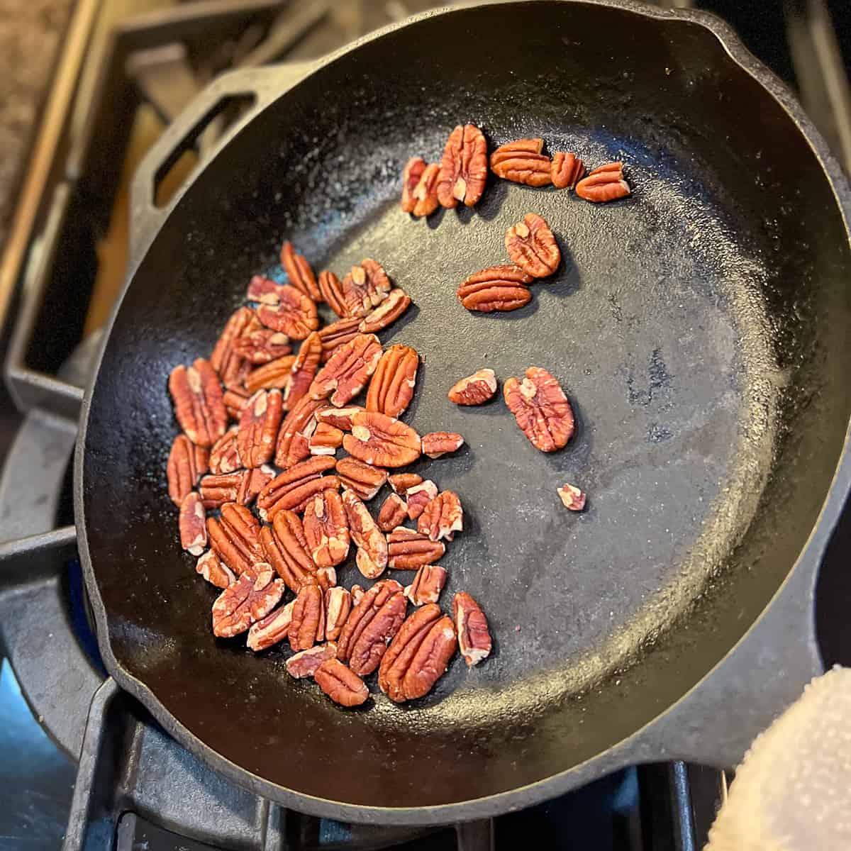 top view of pecans toasting in a cast iron skillet on the stove